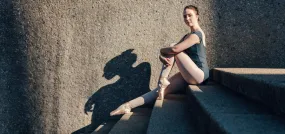 Ballet dancer sitting on stairs wearing pointe shoes.